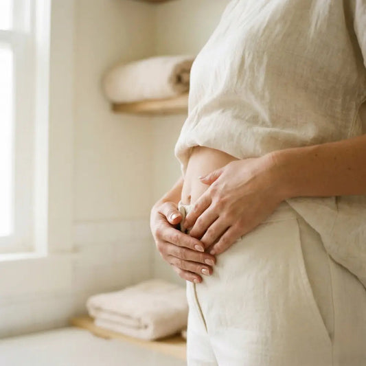 Woman gently resting hands on lower abdomen after c-section, soft natural light in a calm bathroom setting