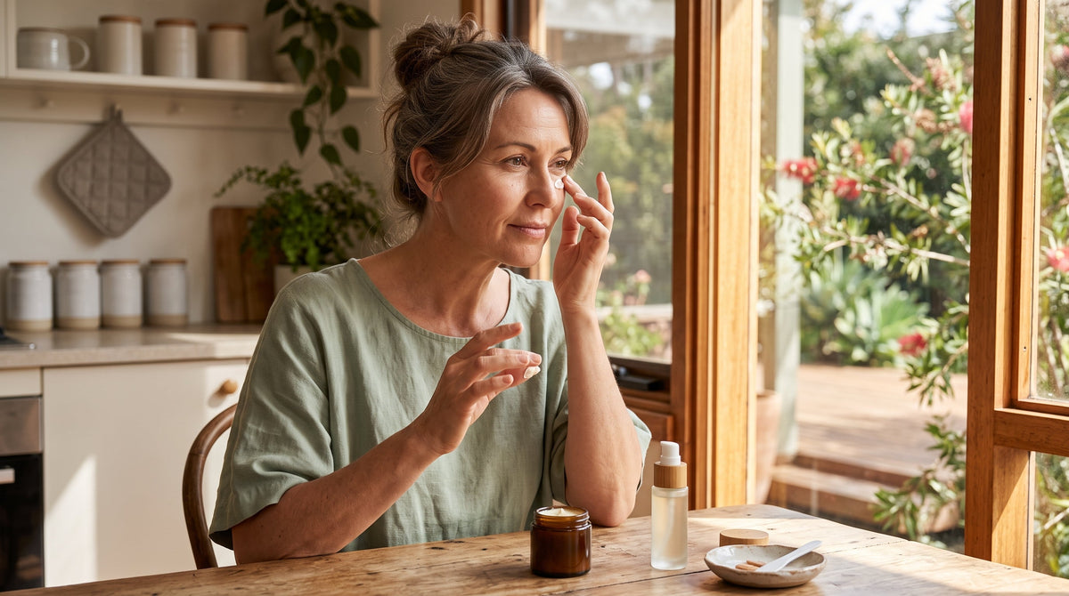 Woman in her late forties dabbing a rich eye cream under her eye with a serum bottle nearby