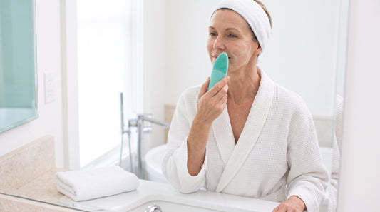 Woman in her fifties gently cleansing her face with a silicone cleansing device at a bathroom basin