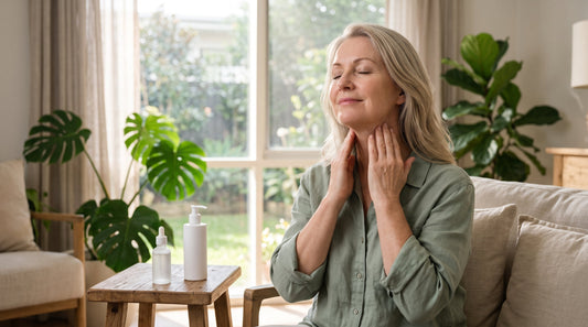 Woman in her fifties smoothing a peptide cream up her neck by a sunny window