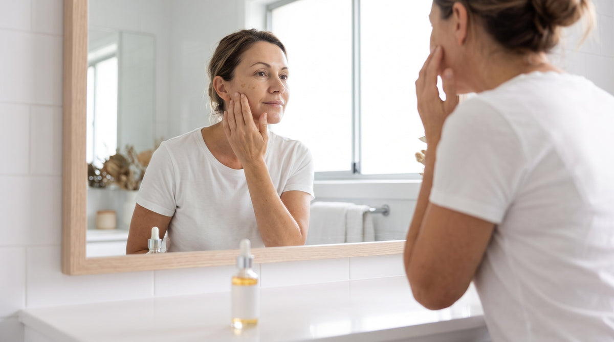 Woman in her fifties checking light sun spots on her cheek in a bathroom mirror