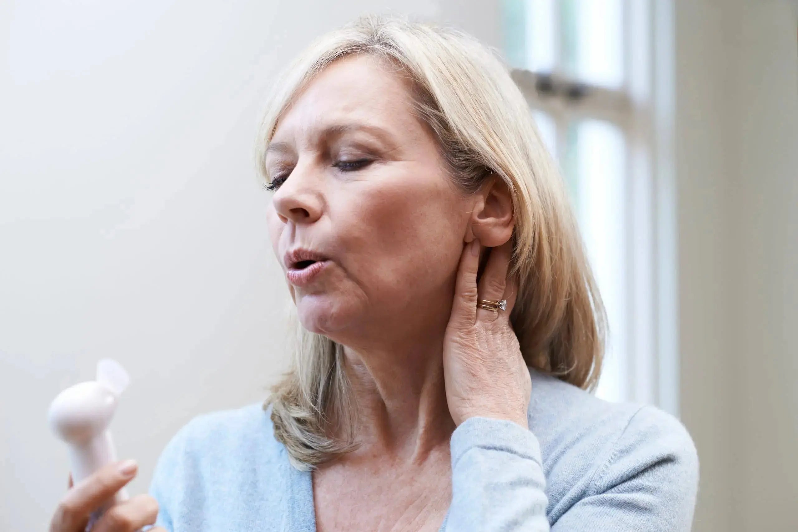 Woman experiencing menopausal hot flush using a handheld fan to cool flushed skin on her face and neck