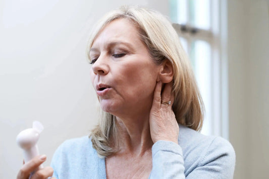 Woman experiencing menopausal hot flush using a handheld fan to cool flushed skin on her face and neck