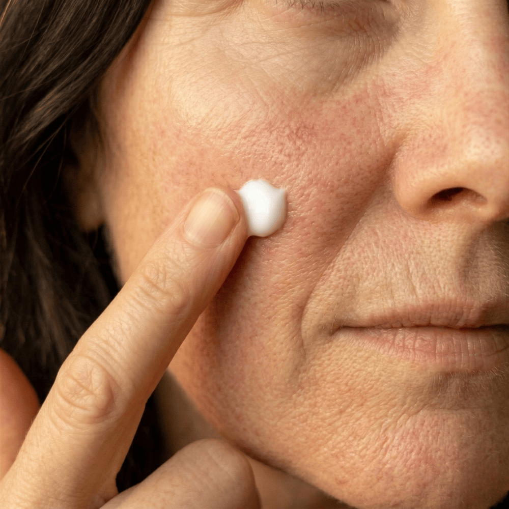 Applying brightening serum to the cheek near the nose on skin with visible pores and uneven pigmentation, targeted skincare for dull menopausal complexion
