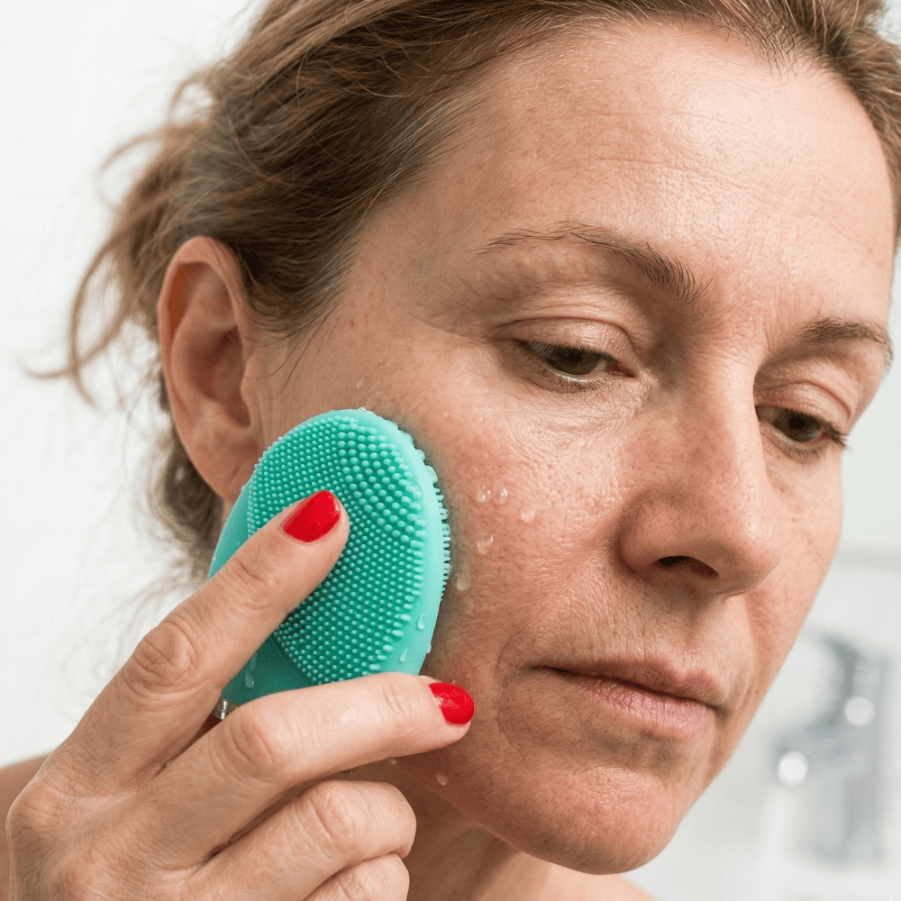 Woman using Genova Personal Silicone Facial Cleanser on cheek with cleansing gel applied, deep pore cleansing to help unclog pores and remove impurities from hormonal and mature skin